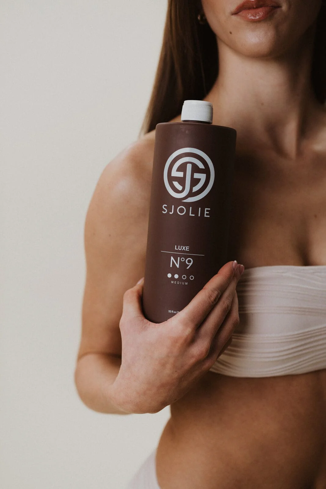 A model holding a bottle of Sjolie Luxe No. 9 spray tan solution