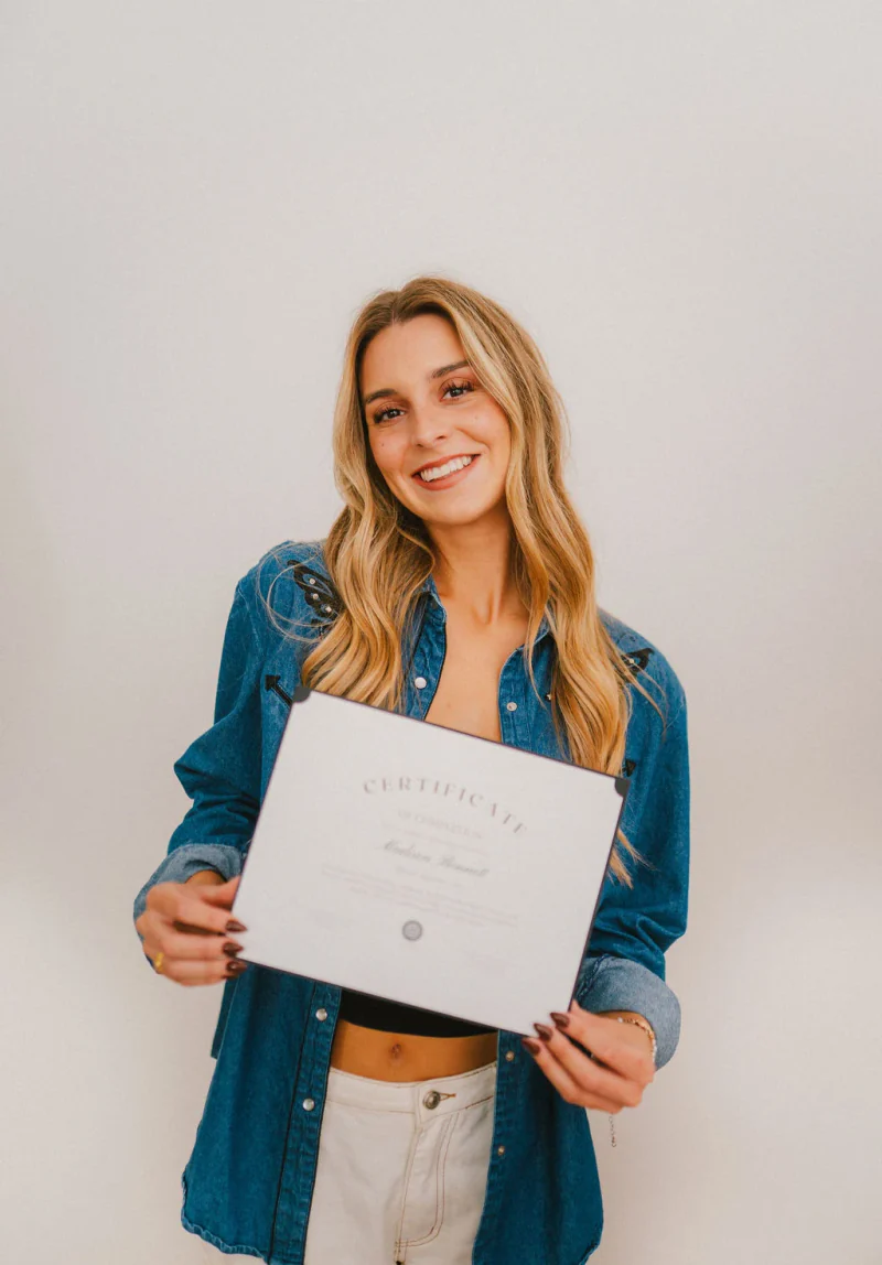 A Sjolie graduate holding her spray tan certification certificate