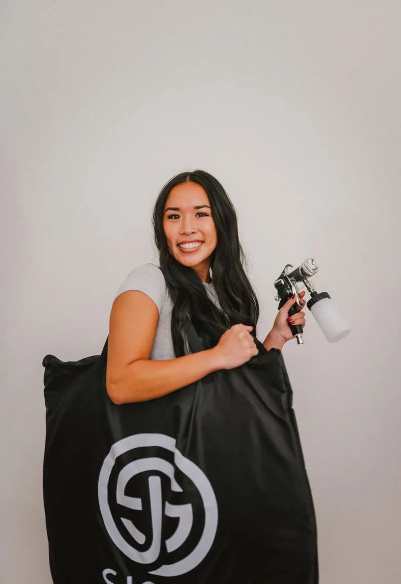 A Sjolie student holding a spray tan applicator and branded equipment bag.