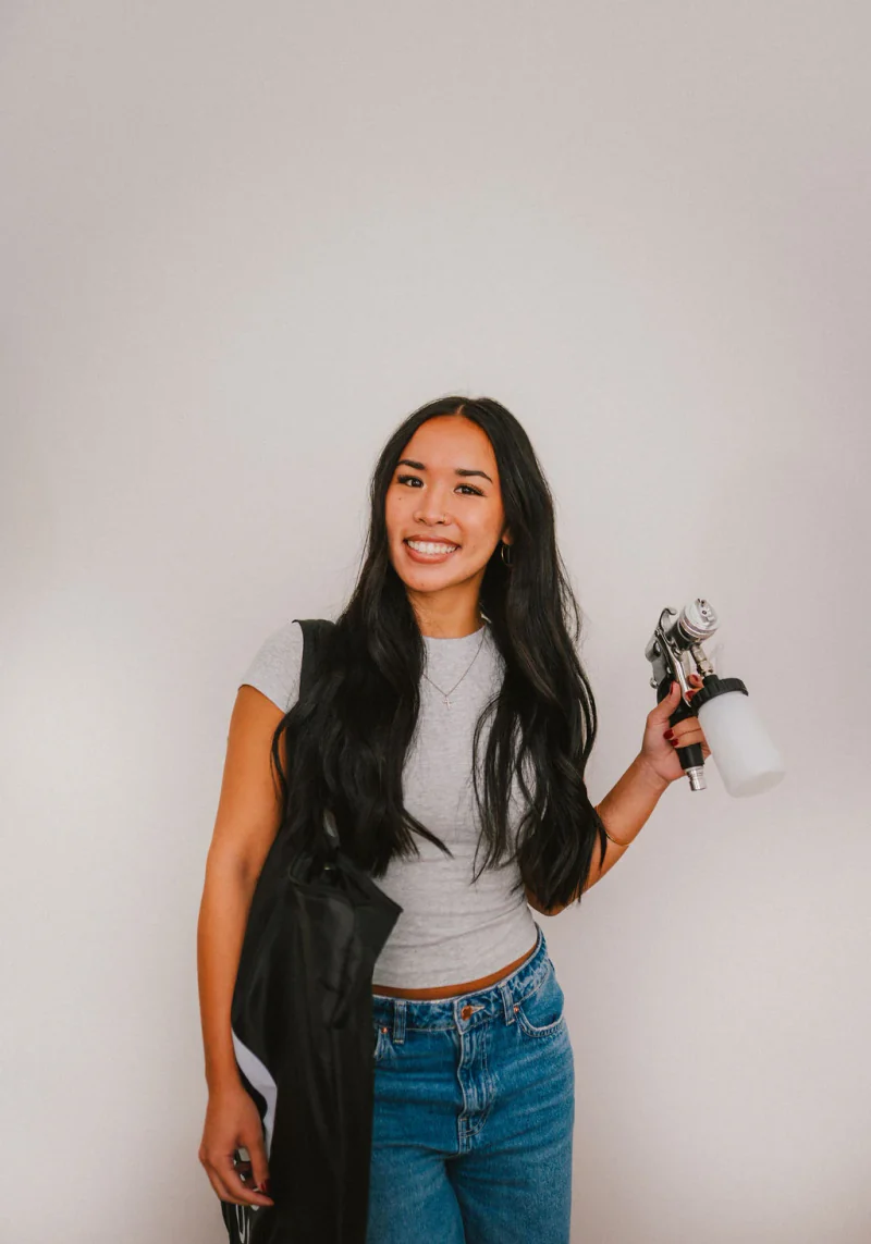 A spray tan course student holding an applicator and equipment bag