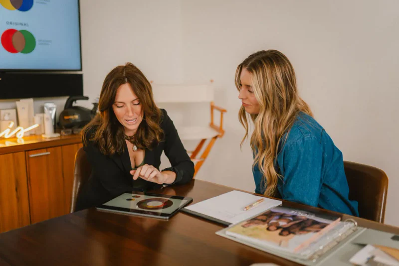 An educator and student reviewing color theory on a tablet with spray tan course materials