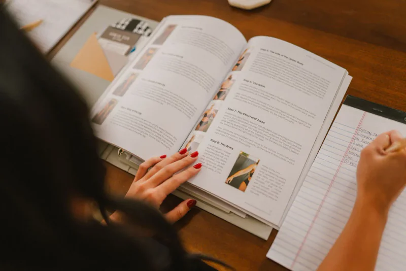 A student taking notes beside an open spray tan training manual